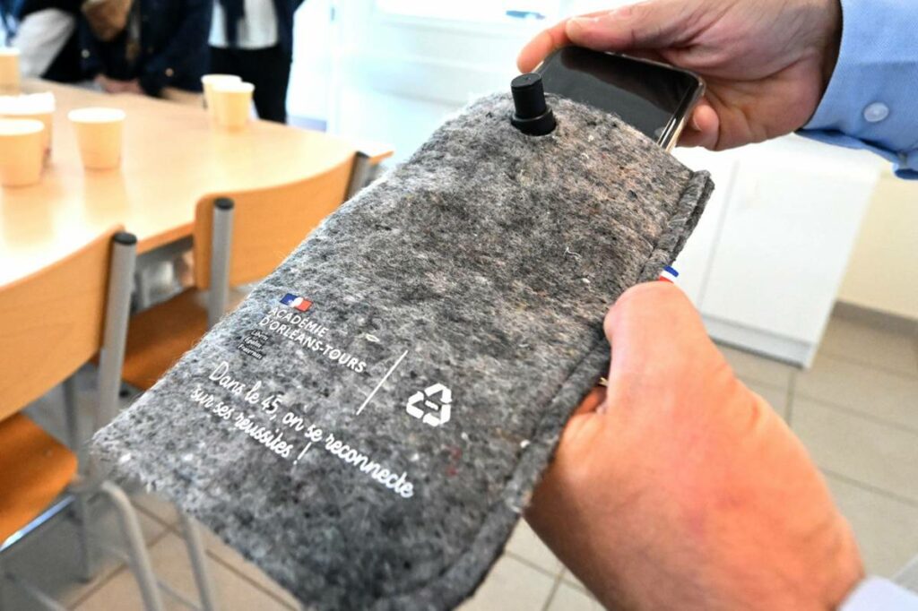 Une photographie d'une pochette dédiée à la pause numérique tenue par une main. L'autre main glisse un téléphone portable dans cette pochette.